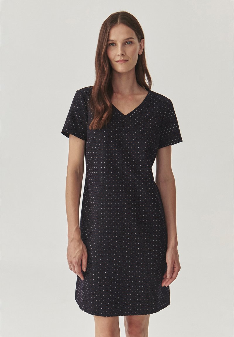 Navy dress with short sleeves, V-neck, and a fitted design. Features a pattern of small, spaced dots in orange. Smooth fabric texture.
