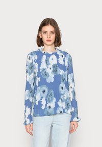 Blusa floral azul com padrões de flores claras e escuras. Mangas longas com punhos fru-fru. Tecido leve e texturizado, decote redondo.