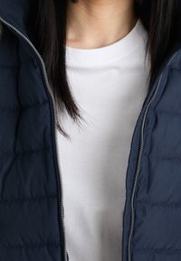 Navy blue puffer vest with a zipper front, featuring a quilted pattern. Underneath, a plain white t-shirt is visible.