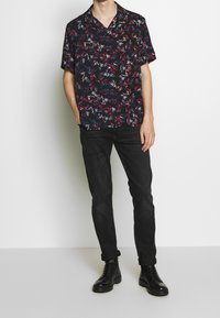 Schwarzes kurzärmeliges Hemd mit Knopfleiste und buntem Blumenmuster. Kombiniert mit dunklen Jeans und schwarzen Schnürstiefeln für einen lässigen Look.