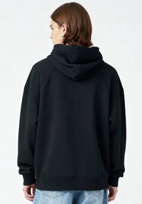 Sweat à capuche noir avec une coupe décontractée, des poignets et un ourlet côtelés, doté d'une texture douce et sans logos ni motifs visibles.