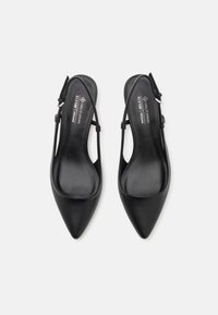 Black vegan leather slingback flats with pointed toes, flat sole, and ankle strap. Smooth texture and minimalistic design.