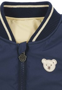 Giubbotto bomber navy con colletto a coste, interno beige e un tirazip a forma di orso, caratterizzato da un orso ricamato bianco sul petto.