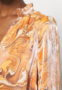 Marbled orange and beige blouse with a silky texture, featuring a ruffled collar and shimmering accents on the fabric.