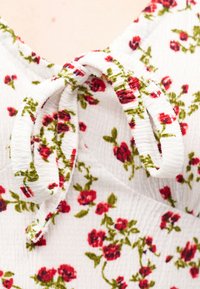 Λευκό φόρεμα με υφή και κόκκινο λουλουδάτο σχέδιο, με έναν δεμένο φιόγκο στον λαιμό.