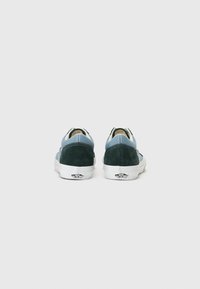 Vans sneakers med en overdel i blå og grønn suede, hvit gummisåle og et distinkt logo på hælen. Bakfra fremheves fargekontrasten.