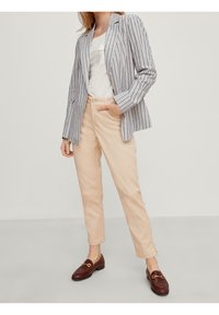 Blazer a rayas en azul y blanco, combinado con pantalones beige. Mocasin marrones con herrajes dorados. Tejido suave y entallado.