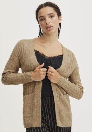 Beige Strickjacke mit geripptem Textur, offener Vorderseite und zwei vorderen Taschen. Getragen über einem schwarzen Oberteil mit Spitzenbesatz und kombiniert mit gestreiften Hosen.