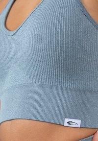 Lichtblauwe geribbelde sportbeha met een brede band en een klein merkaanduiding. De stof heeft een zachte textuur met een aansluitend ontwerp.