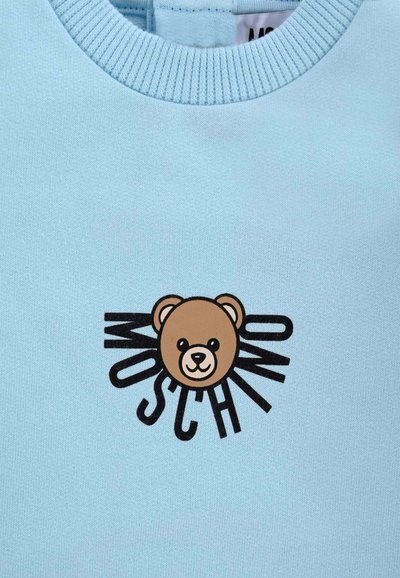 Felpa azzurra chiara con grafica di un orso bruno e un contorno testuale nero "MOSCHINO" che si irradia dal viso dell'orso. Tessuto morbido e testurizzato.