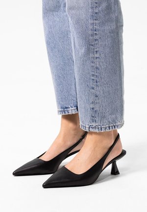 Zwarte leren slingback schoenen met spitse neuzen, lage blokhakken en een open achterkant, gecombineerd met lichtblauwe cropped jeans.