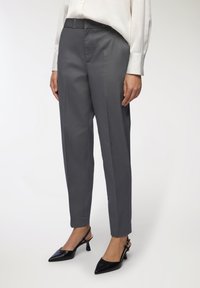 Szare dopasowane spodnie wykonane z gładkiego materiału o luźnym kroju, z płaskim przodem i bocznymi kieszeniami, w połączeniu z czarnymi butami na obcasie typu slingback.