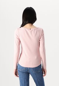 Różowa bluzka z długim rękawem o prążkowanej strukturze, z dekoltem w serek, z poziomym paskiem kontrastowym na plecach oraz zakrzywionym wykończeniem dołu.