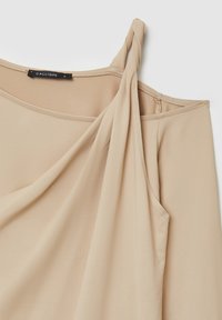 Beige ärmelloses Oberteil aus glattem Stoff, mit einem verdrehten Träger und einem drapierten Design, das sichtbare Nähte aufweist. Markenetikett sichtbar.