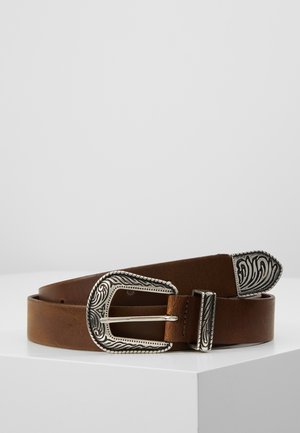Ceinture en cuir marron avec une boucle, un passant et une pointe gravés ton argent, placée enroulée sur une surface blanche sur un fond uni.