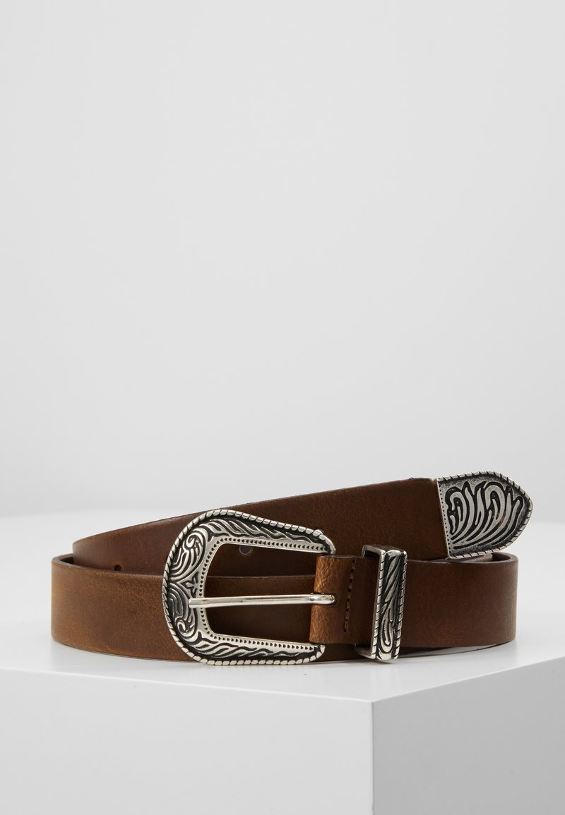 Ceinture en cuir marron avec une boucle, un passant et une pointe gravés ton argent, placée enroulée sur une surface blanche sur un fond uni.