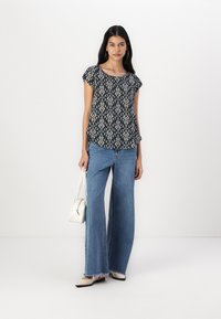 Mørkeblå mønstrete topp med korte ermer, satt sammen med vide denimjeans. Hvit håndveske komplimenterer antrekket og skaper et avslappet utseende.