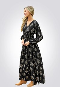 Maxikleid aus schwarzem Stoff mit weißen Blumenmustern, langen Ärmeln mit gerüschten Manschetten, taillierter Taille und schwingendem Rock.