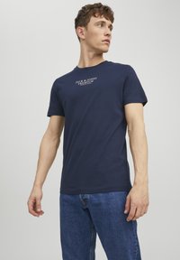 Mornarsko plava pamučna majica s okruglim izrezom i kratkim rukavima, s bijelim natpisom "JACK & JONES PREMIUM" otisnutim sprijeda.