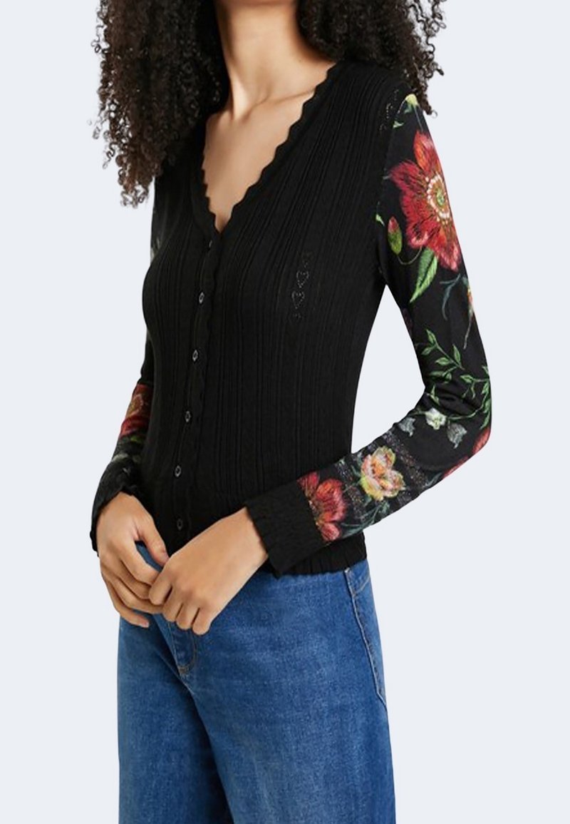 Musta resorineuletakki, jossa on aaltoileva pääntie ja kukkakuvio pitkissä hihoissa. Edessä nappikiinnitys.