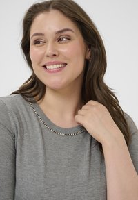 Jersey gris con cuello redondo, que presenta un acento de cuentas plateadas a lo largo del cuello. Textura suave, diseño ligeramente ajustado.