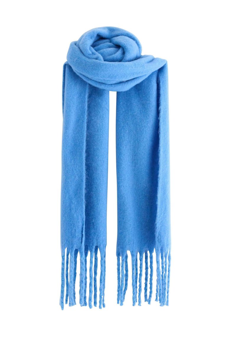 Écharpe en laine bleu clair avec de longs franges, enroulée lâchement sur le dessus, suspendue sur un fond blanc.