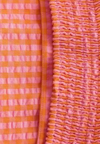 Rosa og orange tekstureret stof med et ternet mønster og smock. Glat finish på den ene side, rynket tekstur på den anden.