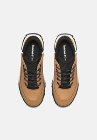 Zapatillas de piel marrón con cordones negros, cuello acolchado y suela texturizada. Presentan un logo en la lengüeta y una entresuela blanca contrastante.