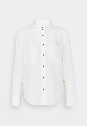 Chemise blanche à manches longues avec col, deux poches avant et boutons marron, présentée sur un fond uni.