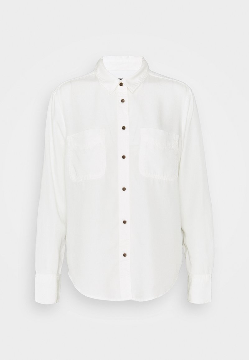 Chemise blanche à manches longues avec col, deux poches avant et boutons marron, présentée sur un fond uni.
