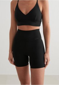 Sujetador deportivo negro sin costuras con diseño en forma de V y pantalones cortos de ciclismo de talle alto a juego. Tela suave y elástica; detalle de marca mínimo.