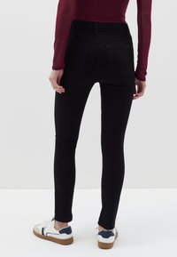 Vaqueros negros ajustados de cintura alta, con dos bolsillos traseros y desgaste mínimo. Combinados con zapatillas blancas con detalles en azul marino.