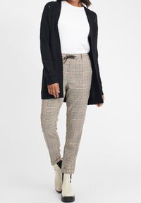 Svart stickad cardigan över en vit t-shirt, tillsammans med rutiga byxor med beiga, svarta och röda accenter. Krämfärgade ankelfötter.