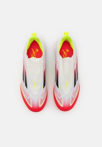 Scarpe da calcio con una tomaia a gradiente bianco e rosa, strisce nere e un colletto giallo brillante. Superficie strutturata e design moderno.