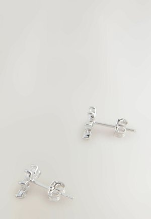 Pari hopeisia nappikorvakoruja, joissa läpinäkyvät suorakaiteen muotoiset jalokivet neutraalilla vaalealla taustalla.