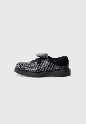 Zapato negro con una textura lisa, que presenta patrones de líneas blancas, un diseño con cordones y una correa de Velcro. Suela de goma gruesa para mayor durabilidad.