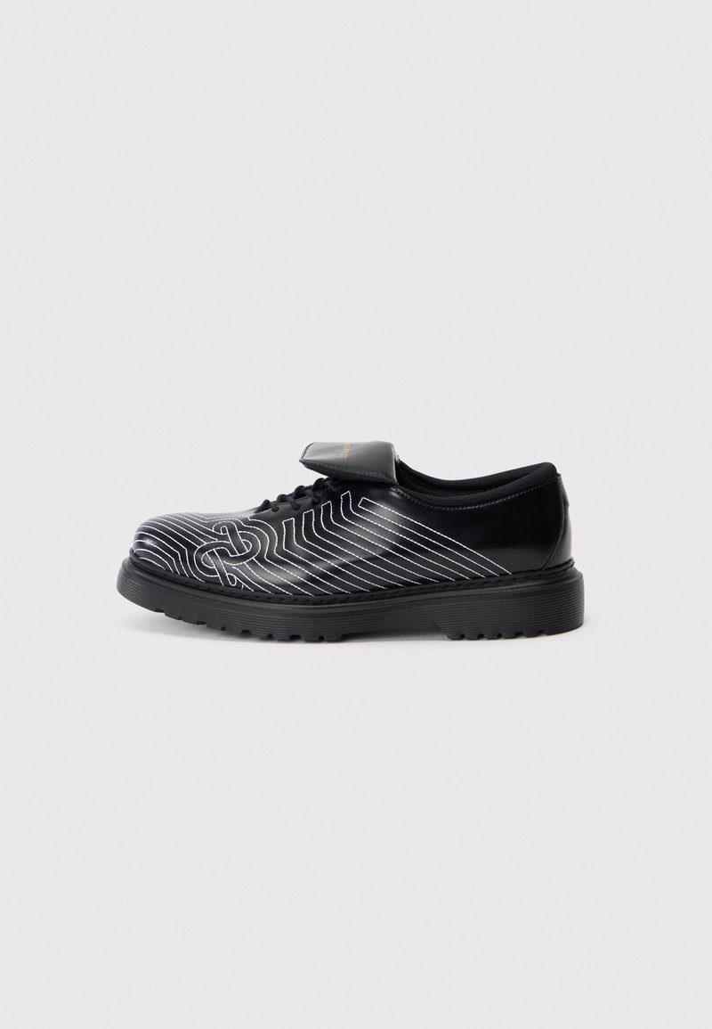 Chaussure noire au texture lisse, ornée de motifs en lignes blanches, conçue avec un laçage et une sangle Velcro. Semelle en caoutchouc épaisse pour une durabilité accrue.