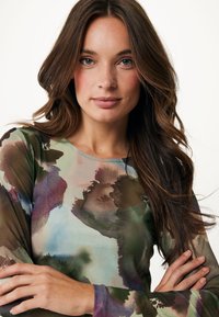 Långärmad topp i genomskinligt, lätt material med ett akvarellblommönster i gröna, bruna och blå nyanser. Slät textur, rund halsringning.