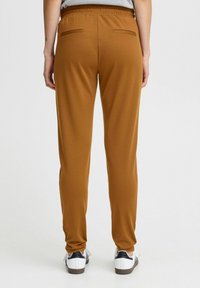 Bruna, tapered joggers tillverkade av ett mjukt material med en stretchig midja och bakfickor, kombinerade med vita skor med svarta detaljer.