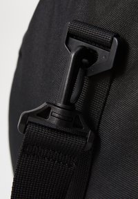 Correa de nailon negra con un conector de hebilla de plástico y superficie texturizada, que muestra un material duradero y un mecanismo de cierre seguro.