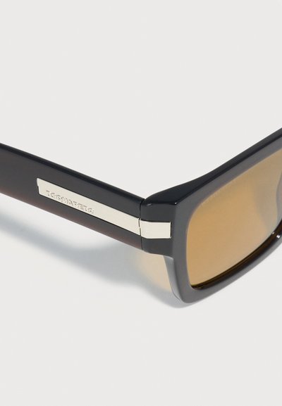 Μαύρα ορθογώνια γυαλιά ηλίου με φακούς καφέ απόχρωσης και ασημί μεταλλική λεπτομέρεια στο πλάι.
