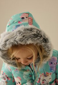 Tyrkysová péřová bunda se barevnými kreslenými postavičkami, s měkkou šedou umělou kožešinovou kapucí a zipovým uzávěrem.
