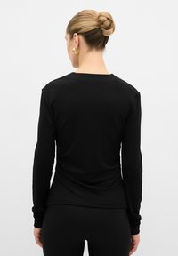 Maglietta nera a maniche lunghe con un design aderente, texture liscia e scollo rotondo, caratterizzata da leggere arricciature sul retro.