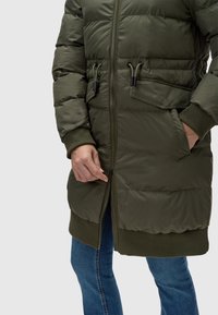 Khaki prešívaný kabát so zipsom, rebrovanými manžetami a sťahovacími detailmi v oblasti pása. Jedna vrecko na ľavej strane.