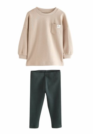 Vaalean beige pitkähihaisessa paidassa on rintatasku, ja se on yhdistetty tummanvihreisiin ribbihousuihin, jotka on valmistettu pehmeästä kankaasta. Yksinkertainen, mukava muotoilu.