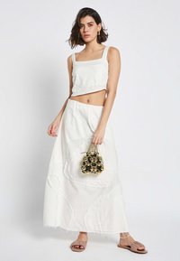 Weißes, kurzes Oberteil mit quadratischem Ausschnitt, kombiniert mit einem hoch taillierten Rock, der strukturierte Blumenmuster aufweist. Accessoires umfassen eine kleine schwarze Tasche.