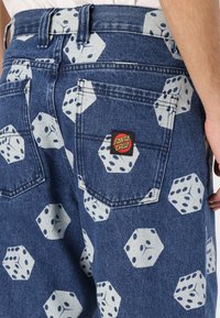 Denim shorts with a blue wash, featuring a white dice pattern and a red SANTA CRUZ logo patch on the back pocket.