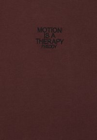 Camiseta de algodón burdeos con texto bordado en negro que dice "MOTION IS A THERAPY FREDDY" cerca del lado superior izquierdo.