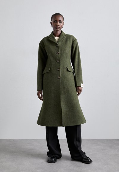 Manteau en laine vert à la coupe ajustée, avec de gros boutons sur le devant et deux poches latérales, présentant un col haut et un ourlet évasé.