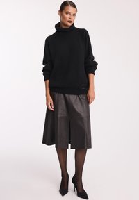 Czarny, oversize sweter dzianinowy z wysokim kołnierzem, w połączeniu z czarną skórzaną spódnicą do kolan z detalami plis na przodzie oraz czarnymi szpilkami.